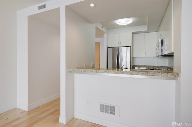 kitchen featuring white cabinets, light wood-type flooring, light stone countertops, and appliances with stainless steel finishes