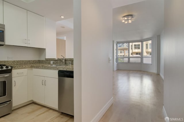 kitchen with light stone countertops, white cabinets, stainless steel appliances, light hardwood / wood-style floors, and sink