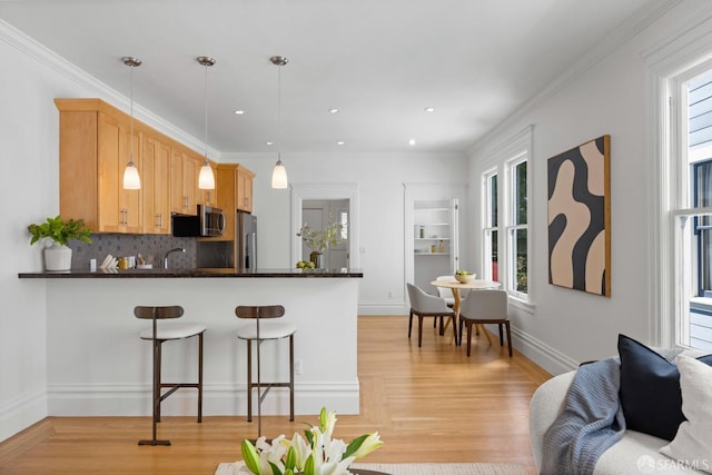 kitchen with appliances with stainless steel finishes, healthy amount of natural light, dark countertops, a breakfast bar, and ornamental molding