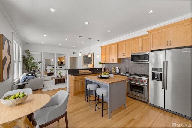 kitchen with appliances with stainless steel finishes, a peninsula, a sink, backsplash, and light wood-style floors