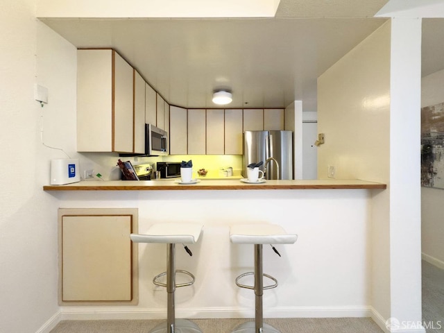 kitchen featuring stainless steel appliances, kitchen peninsula, a kitchen bar, light carpet, and cream cabinetry