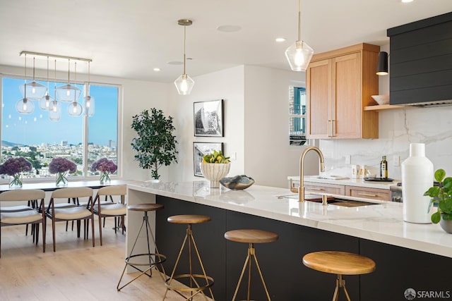 kitchen featuring light stone counters, a sink, decorative backsplash, a kitchen bar, and decorative light fixtures