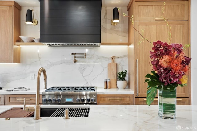 kitchen featuring wall chimney range hood, a sink, light stone counters, and decorative backsplash