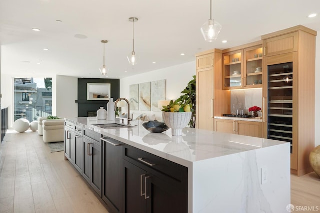 kitchen with decorative light fixtures, open floor plan, light brown cabinets, a sink, and light stone countertops