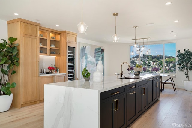 kitchen featuring dark cabinets, a sink, a center island with sink, glass insert cabinets, and pendant lighting