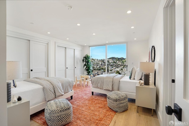 bedroom with expansive windows, wood finished floors, two closets, and recessed lighting