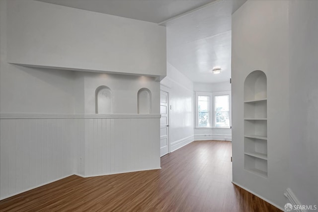 unfurnished living room featuring built in shelves and dark hardwood / wood-style floors