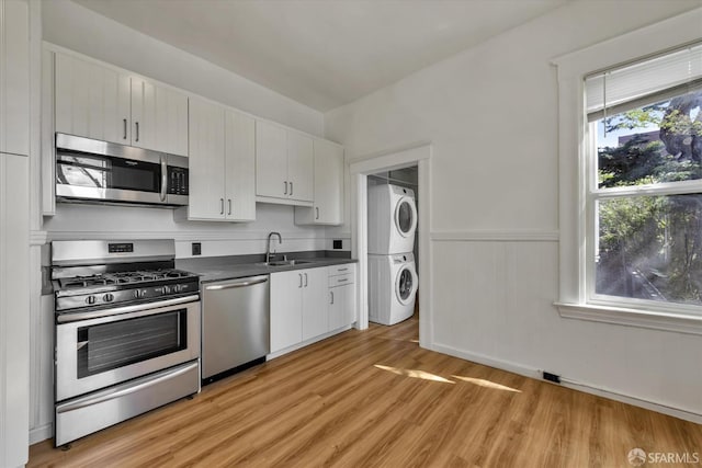 kitchen with appliances with stainless steel finishes, sink, light hardwood / wood-style flooring, white cabinets, and stacked washer and dryer