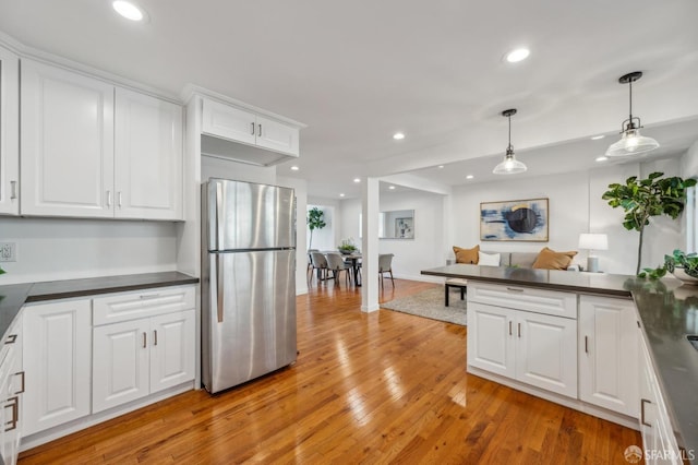 kitchen featuring white cabinets, light wood finished floors, dark countertops, freestanding refrigerator, and pendant lighting
