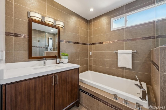 bathroom with vanity, a relaxing tiled tub, and tile walls