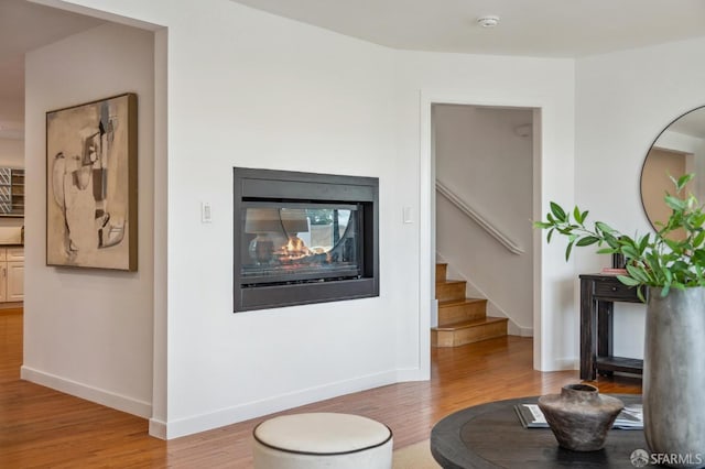 living area featuring baseboards, a multi sided fireplace, wood finished floors, and stairs