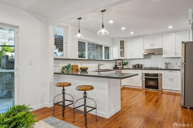 kitchen with light wood-style flooring, dark countertops, white cabinetry, under cabinet range hood, and appliances with stainless steel finishes