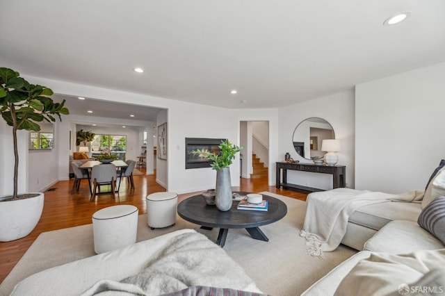 living room with stairs, a glass covered fireplace, wood finished floors, and recessed lighting