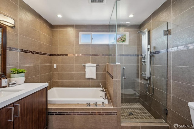 bathroom featuring toilet, tile walls, a stall shower, a garden tub, and vanity