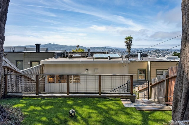 rear view of property featuring roof mounted solar panels, a lawn, fence, and a mountain view