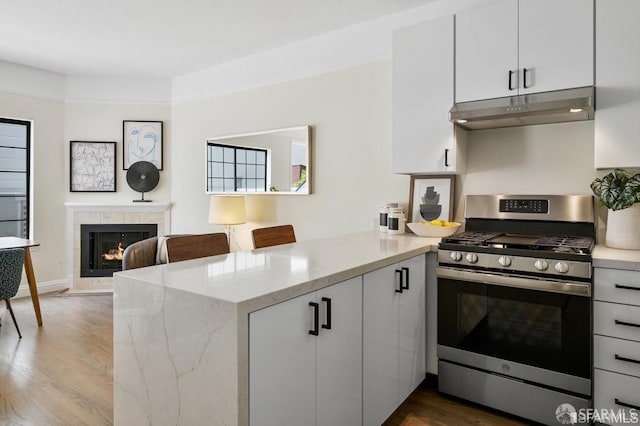 kitchen featuring dark wood-type flooring, white cabinets, kitchen peninsula, a high end fireplace, and stainless steel range with gas stovetop