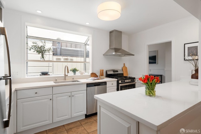 kitchen with wall chimney range hood, light tile patterned floors, sink, appliances with stainless steel finishes, and white cabinets