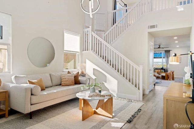 living room with a high ceiling, ceiling fan, a barn door, and light wood-type flooring