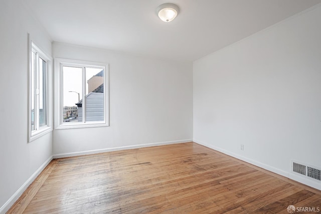empty room featuring light wood-style floors, visible vents, and baseboards