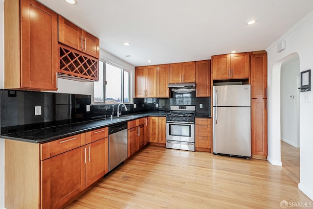 kitchen featuring light wood finished floors, under cabinet range hood, stainless steel appliances, a sink, and arched walkways