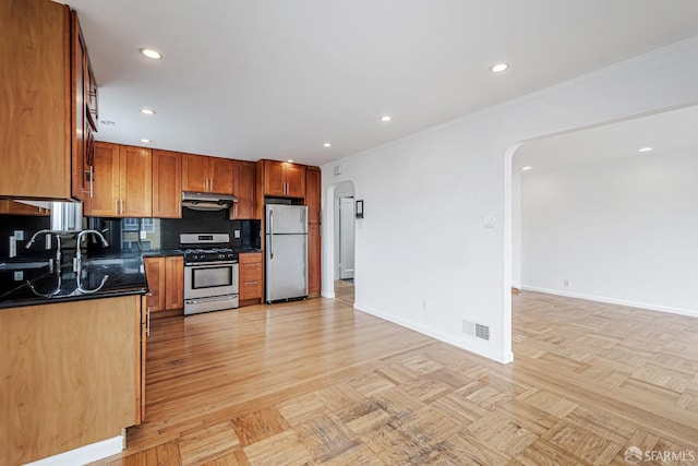 kitchen featuring under cabinet range hood, dark countertops, visible vents, arched walkways, and appliances with stainless steel finishes
