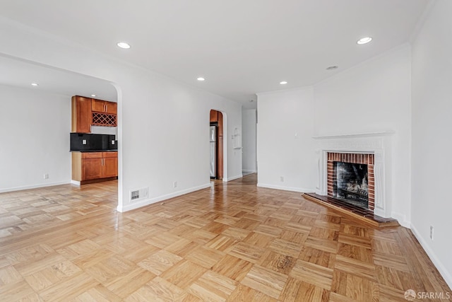 unfurnished living room with recessed lighting, visible vents, arched walkways, baseboards, and a fireplace