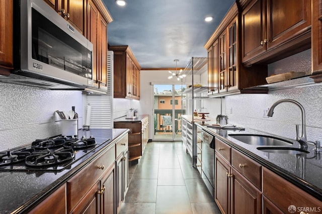 kitchen featuring an inviting chandelier, appliances with stainless steel finishes, dark stone counters, ornamental molding, and sink