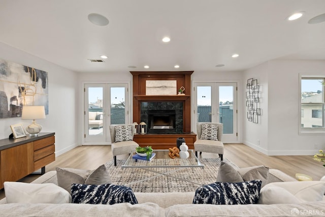 living room featuring light wood-type flooring, a fireplace, a water view, and french doors