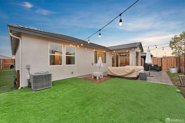 back house at dusk with central AC, a patio area, and a lawn