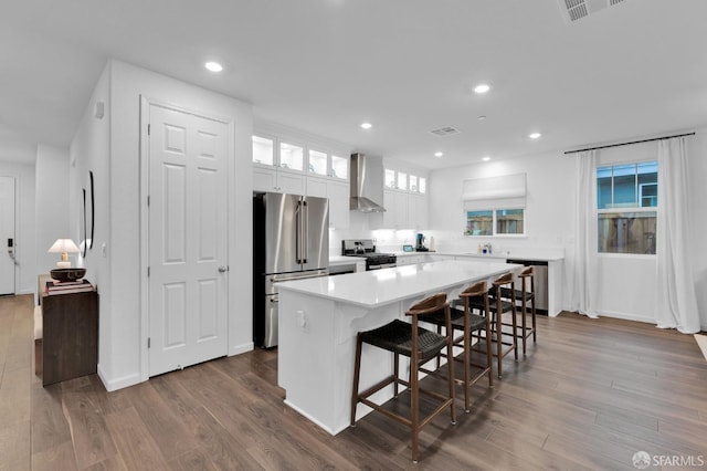 kitchen featuring a kitchen island, appliances with stainless steel finishes, a breakfast bar, white cabinetry, and wall chimney exhaust hood