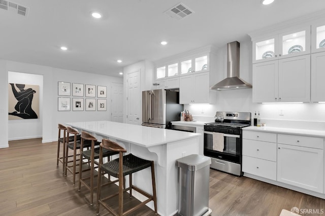 kitchen featuring white cabinets, stainless steel appliances, a center island, and wall chimney range hood