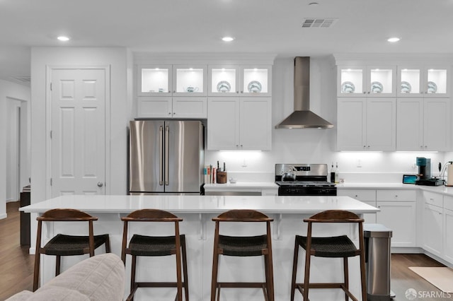 kitchen with appliances with stainless steel finishes, white cabinetry, a kitchen bar, a center island, and wall chimney range hood