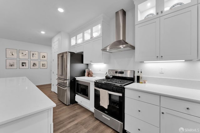 kitchen with wall chimney range hood, hardwood / wood-style floors, white cabinets, and appliances with stainless steel finishes