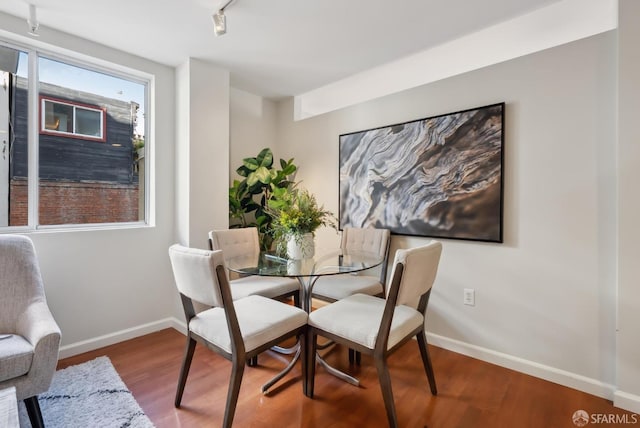 dining space with track lighting, baseboards, and wood finished floors