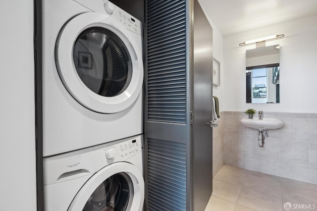 laundry area with stacked washer / drying machine, light tile patterned floors, sink, and tile walls