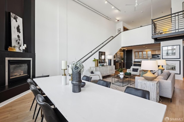 dining area featuring ceiling fan, a fireplace, a high ceiling, and light hardwood / wood-style flooring