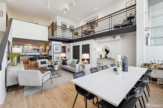 dining space featuring ceiling fan, light hardwood / wood-style floors, a towering ceiling, and track lighting