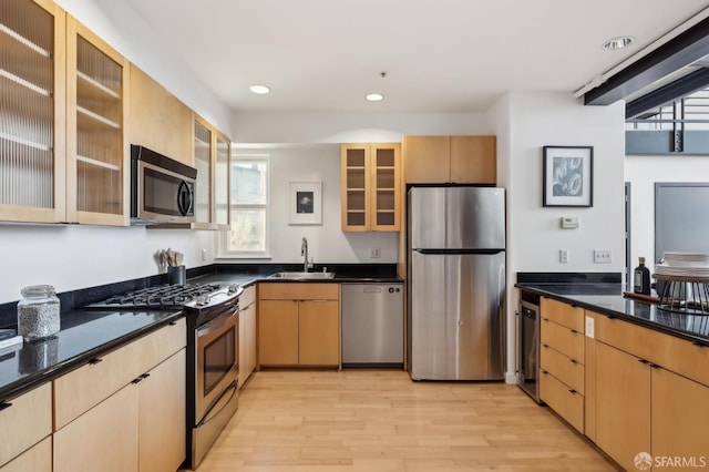 kitchen featuring light brown cabinetry, stainless steel appliances, sink, light hardwood / wood-style flooring, and dark stone countertops