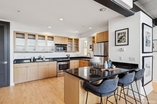 kitchen with light brown cabinets, stainless steel appliances, light hardwood / wood-style flooring, kitchen peninsula, and a kitchen bar