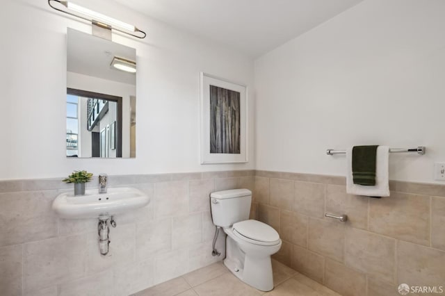 bathroom featuring toilet, tile patterned floors, tile walls, and sink