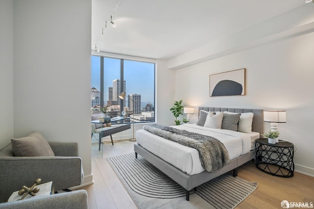 bedroom with light hardwood / wood-style flooring, a wall of windows, and track lighting