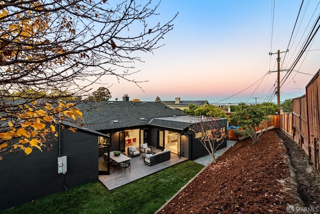 back house at dusk with an outdoor living space, a lawn, and a patio area