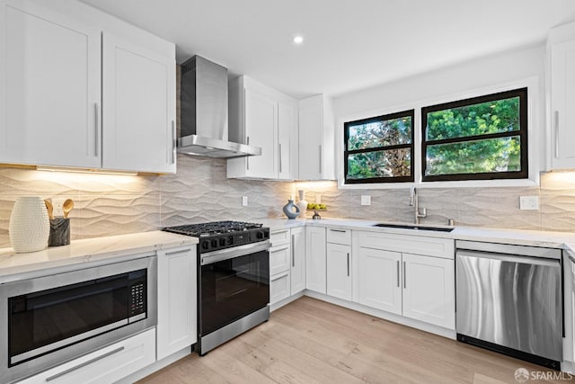 kitchen with white cabinetry, wall chimney range hood, sink, and appliances with stainless steel finishes