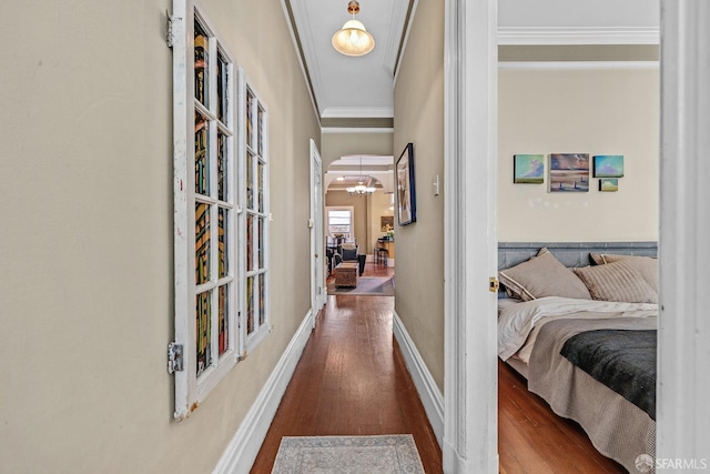 hallway featuring arched walkways, ornamental molding, wood finished floors, and baseboards