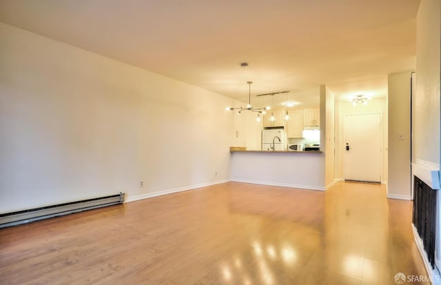 unfurnished living room with a notable chandelier, baseboard heating, and light wood-type flooring