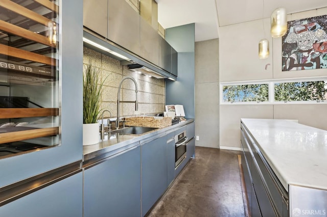 kitchen with hanging light fixtures, blue cabinets, backsplash, oven, and sink