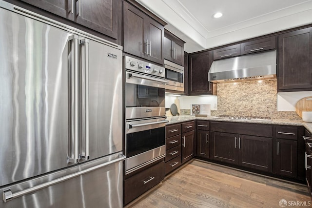 176 Summit Way, San Francisco, CA 94132 - kitchen featuring appliances with stainless steel finishes, exhaust hood, dark brown cabinets, light wood-style flooring, and light stone countertops