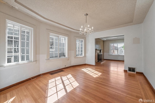 unfurnished dining area featuring a brick fireplace, a notable chandelier, visible vents, and wood finished floors