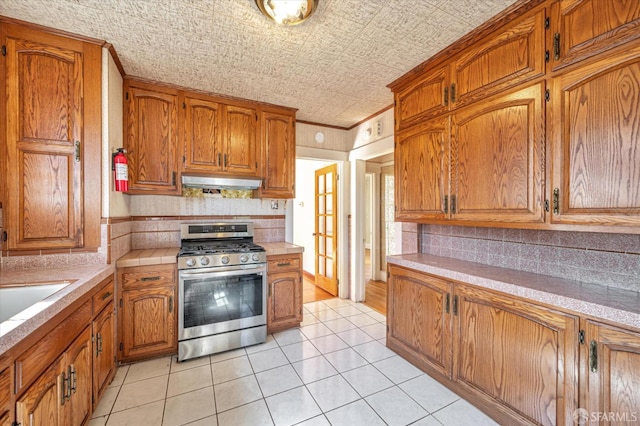 kitchen with an ornate ceiling, brown cabinets, stainless steel gas stove, and under cabinet range hood