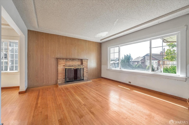 unfurnished living room featuring a fireplace, light wood finished floors, wooden walls, a textured ceiling, and baseboards